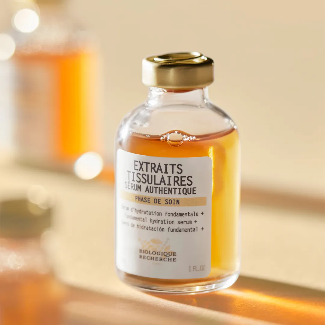 Скляний флакон сироватки Extraits Tissulaires Biologique Recherche із золотистою кришкою в сонячному світлі